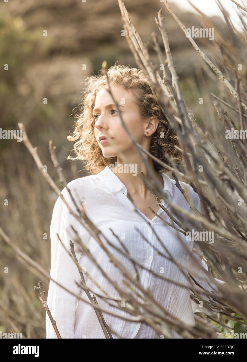 Giovane attraente Donna affascinante vicino rami secchi di arbusto su sfondo sfocato Foto Stock