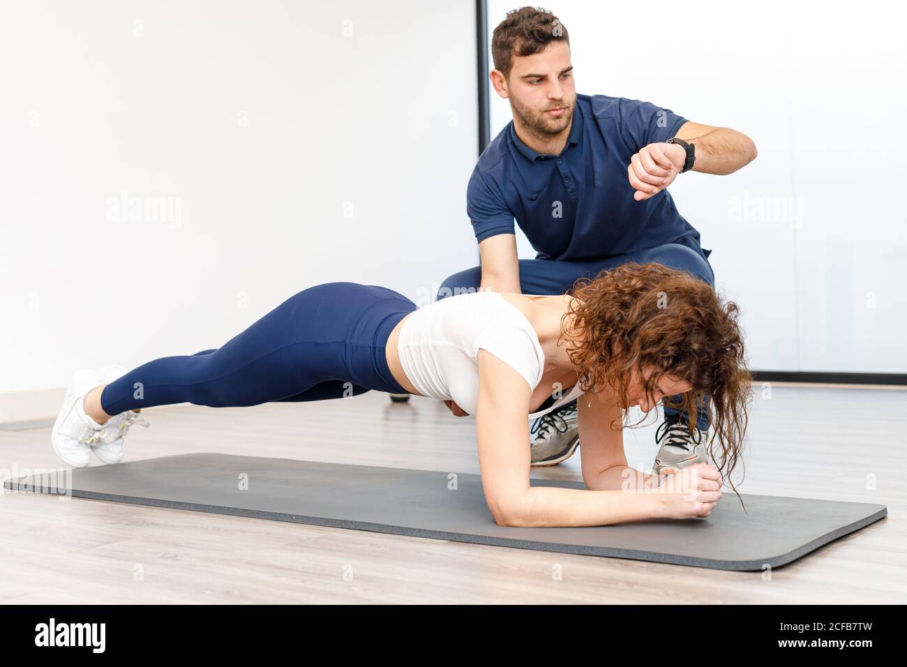 Lady facendo esercizio in tavola con istruttore personale in palestra Foto Stock
