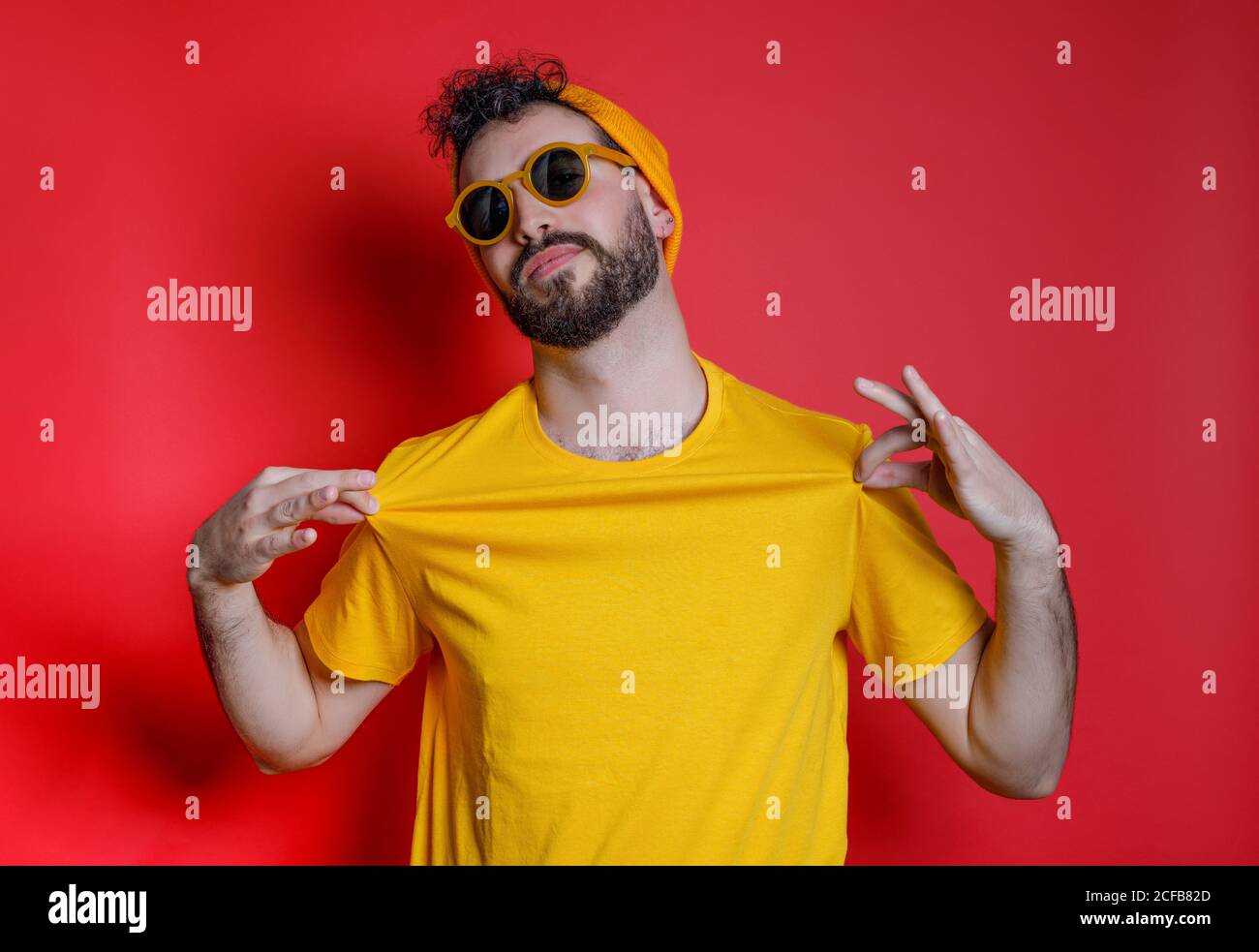 Uomo trendy con bearded in camicia di tenuta gialla in piedi contro Bright sfondo giallo che guarda la fotocamera Foto Stock
