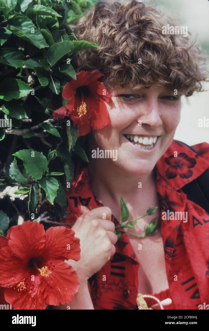 Giovane donna in piedi accanto all'albero fiorito di Hibiscus Foto Stock