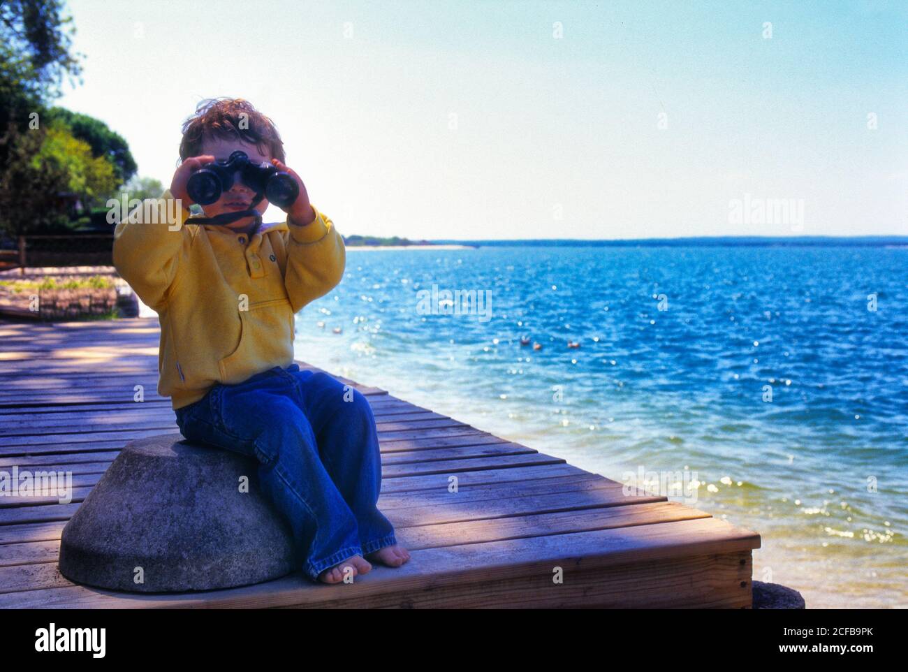 Bambino bambino che guarda attraverso binocoli, al bordo delle acque Foto Stock