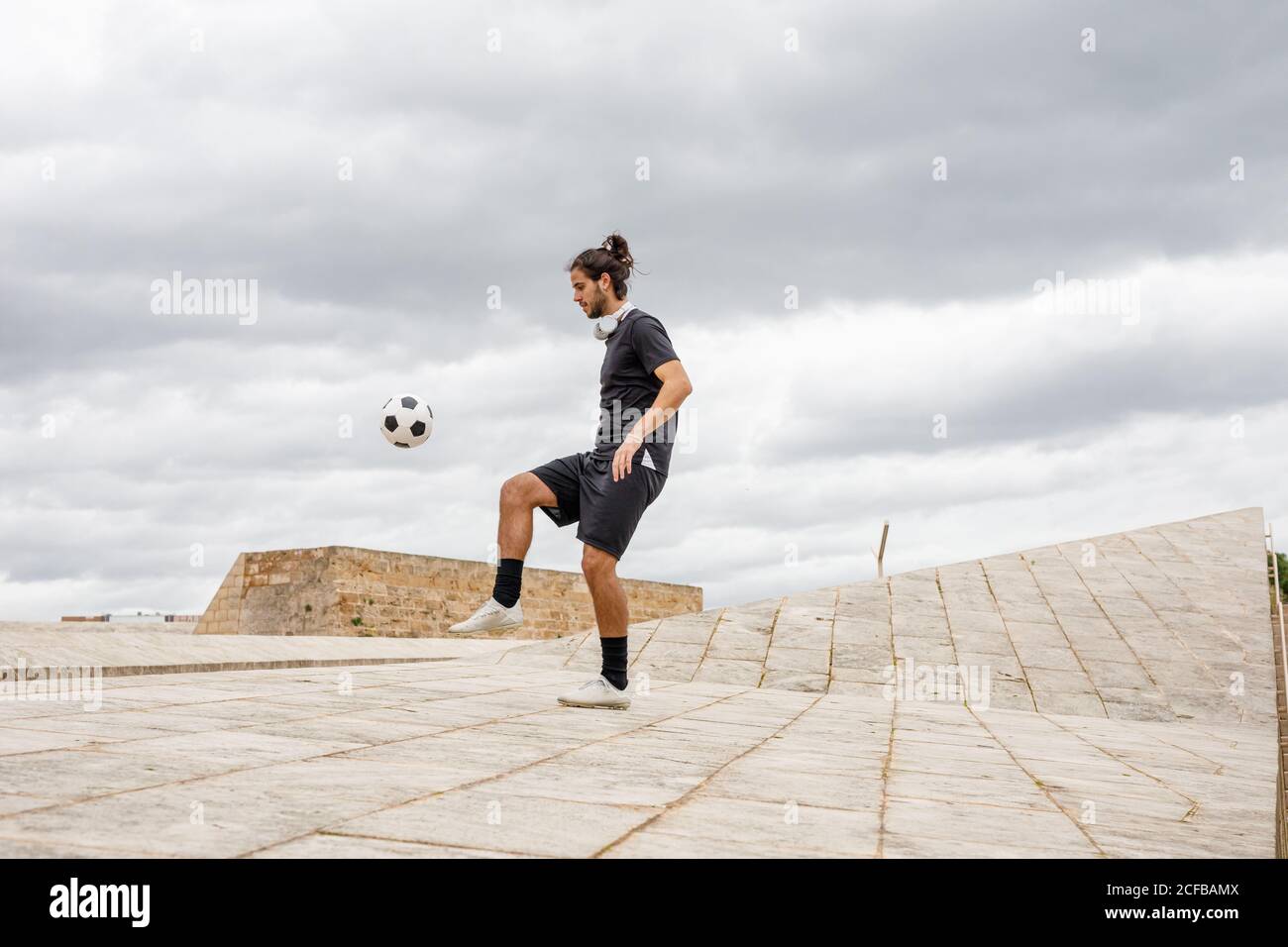 uomo allenarsi con palla di calcio contro cielo nuvoloso Foto Stock