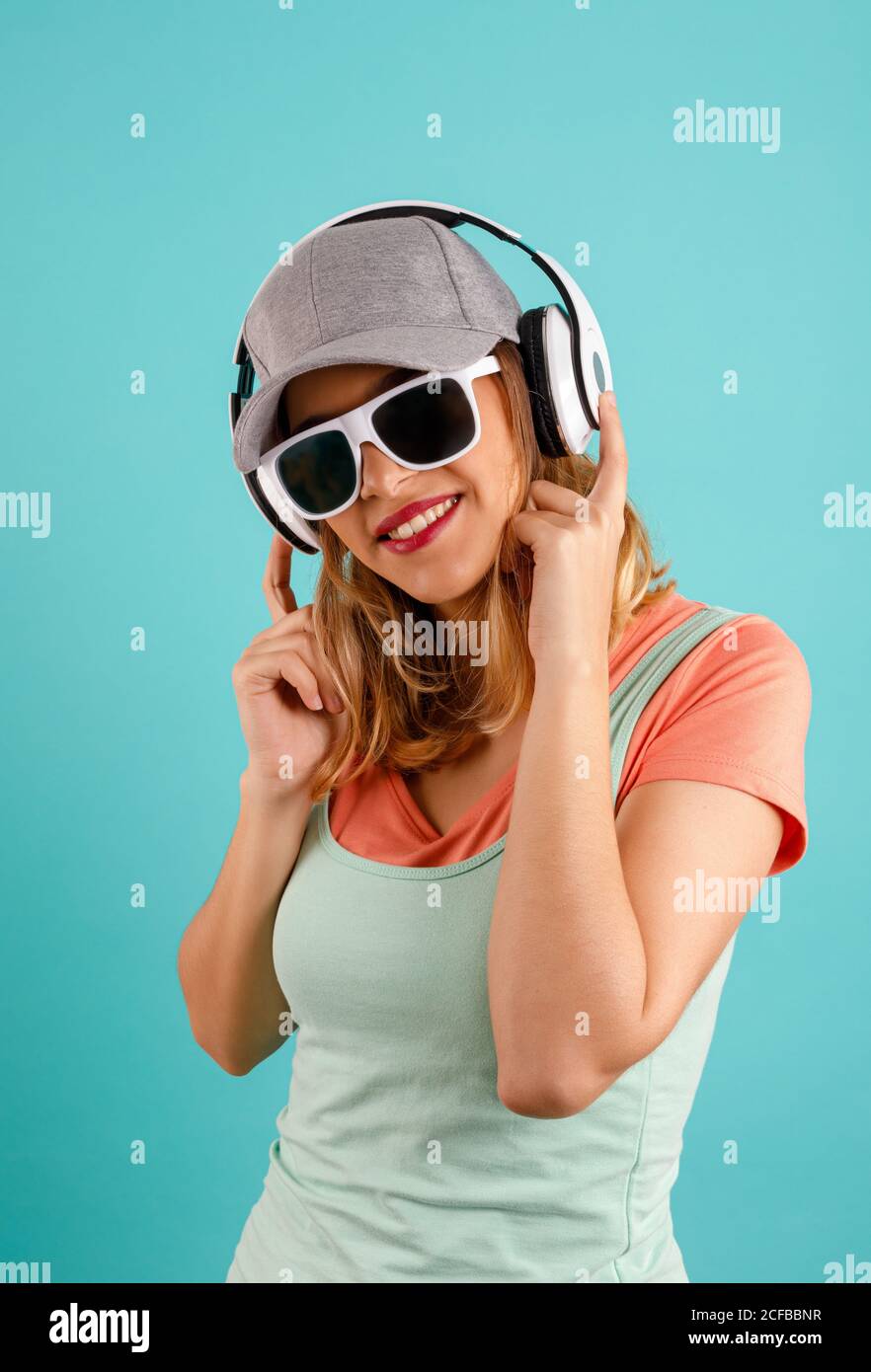 Giovane donna in eleganti occhiali da sole e cuffie che toccano il  cappuccio e. guardare la fotocamera mentre si ascolta la musica su sfondo  turchese Foto stock - Alamy