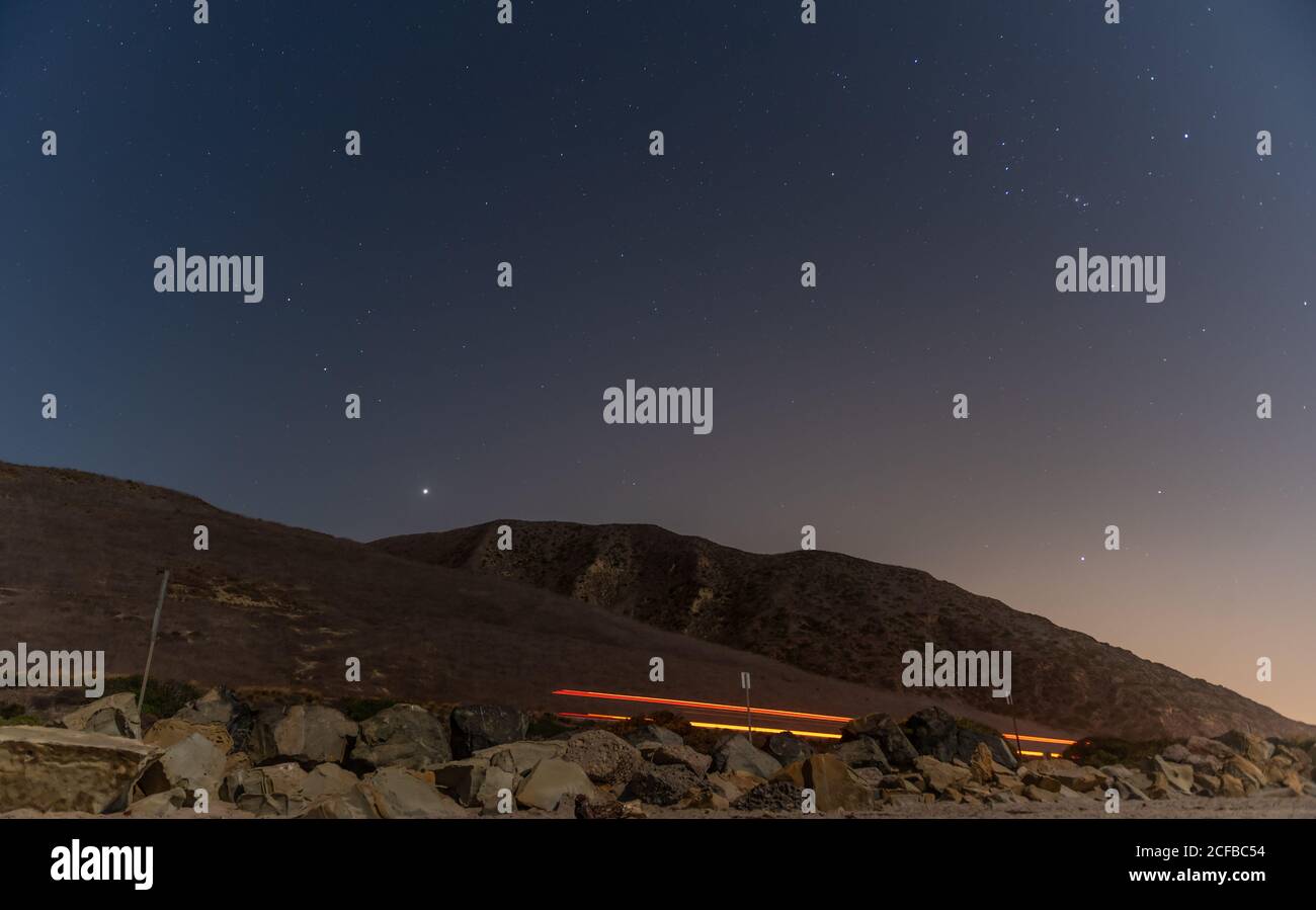Fari striati sulla strada sottostante e luminosa costellazione di Orion e altre stelle contro un cielo notturno. Foto Stock