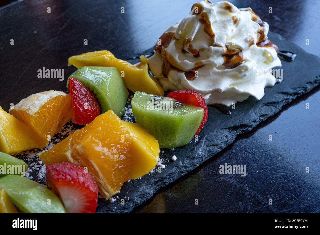 Kebab di frutta fatto di arance, fragole, Kiwi, Mango servito con panna montata. Primo piano della macro. Messa a fuoco selettiva Foto Stock