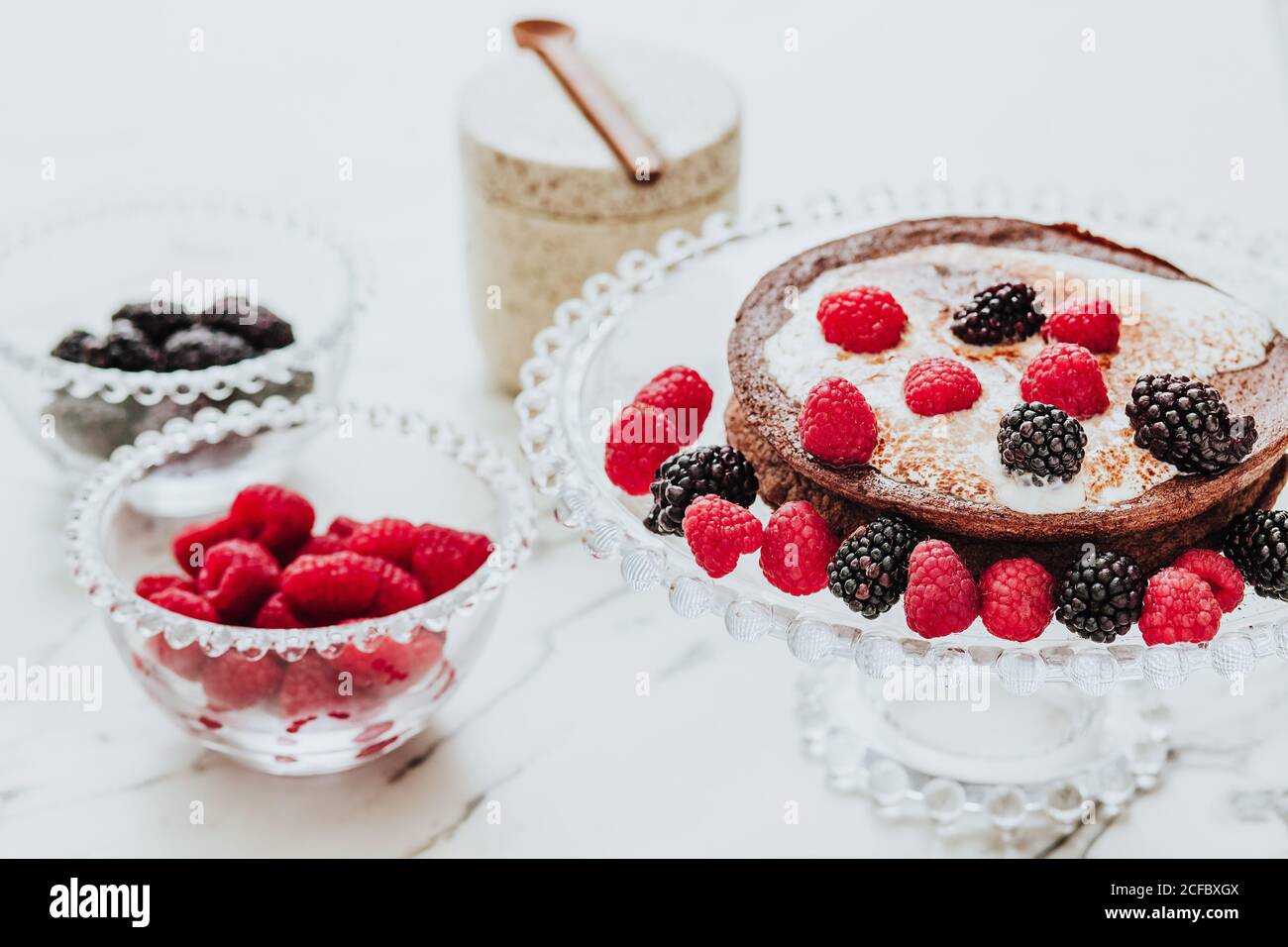 Angolo di gustosa crostata dolce con ripieno cremoso e. blackberry fresco e lampone su vetro stand in composizione con ciotole di bacche fresche Foto Stock