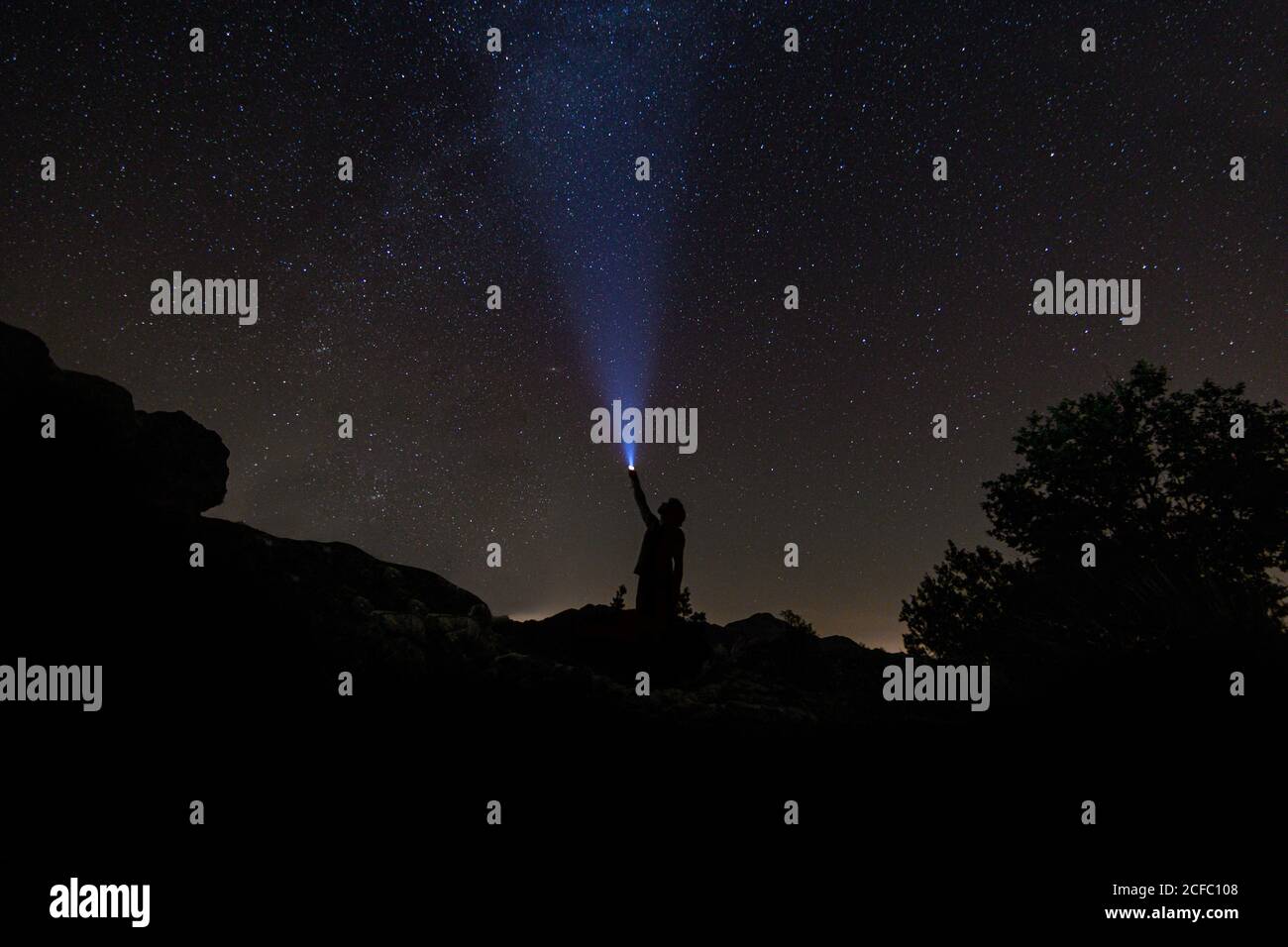 Cielo notturno con la silhouette di un uomo che si illumina con una torcia elettrica Foto Stock