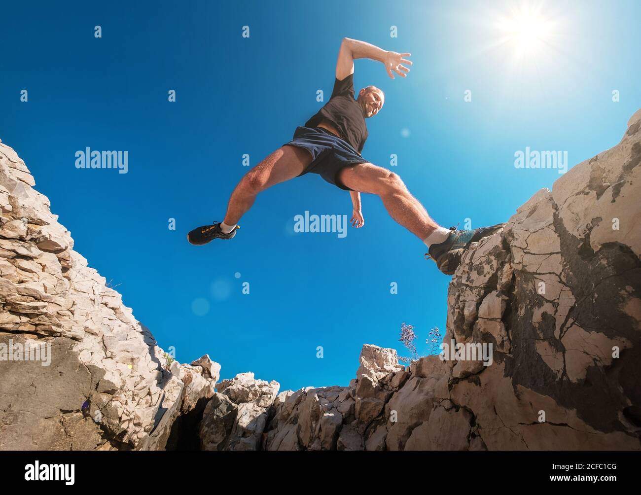 Attivo veloce running montagna Sky runner sorridente e saltando sopra la scogliera scagliata durante il jogging mattutino. Attività sportive per le persone con un ampio angolo di climatizzazione Foto Stock