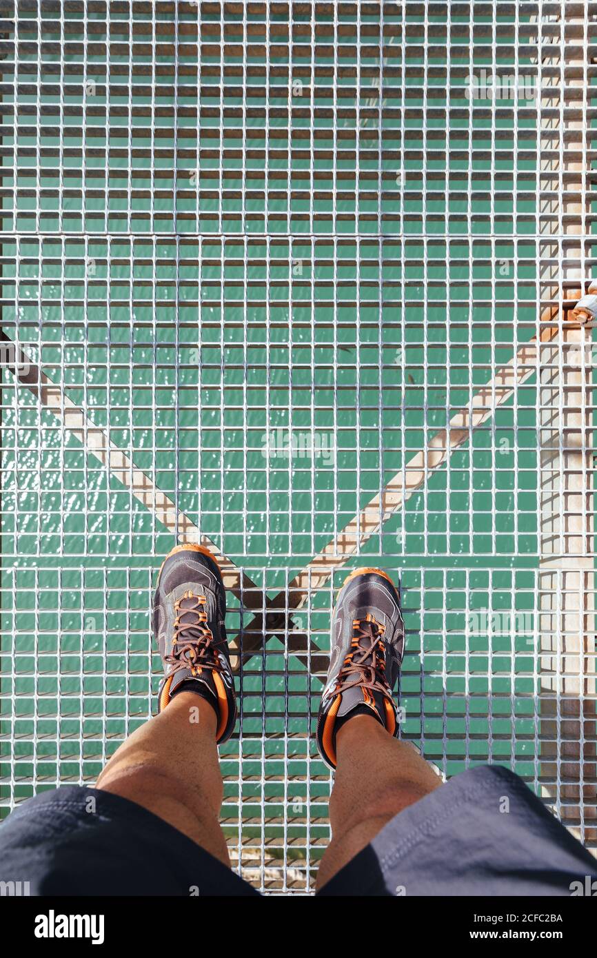 Vista dall'alto delle gambe dell'uomo irriconoscibili che si erigano su un ponte di montagna sopra un fiume. Foto Stock