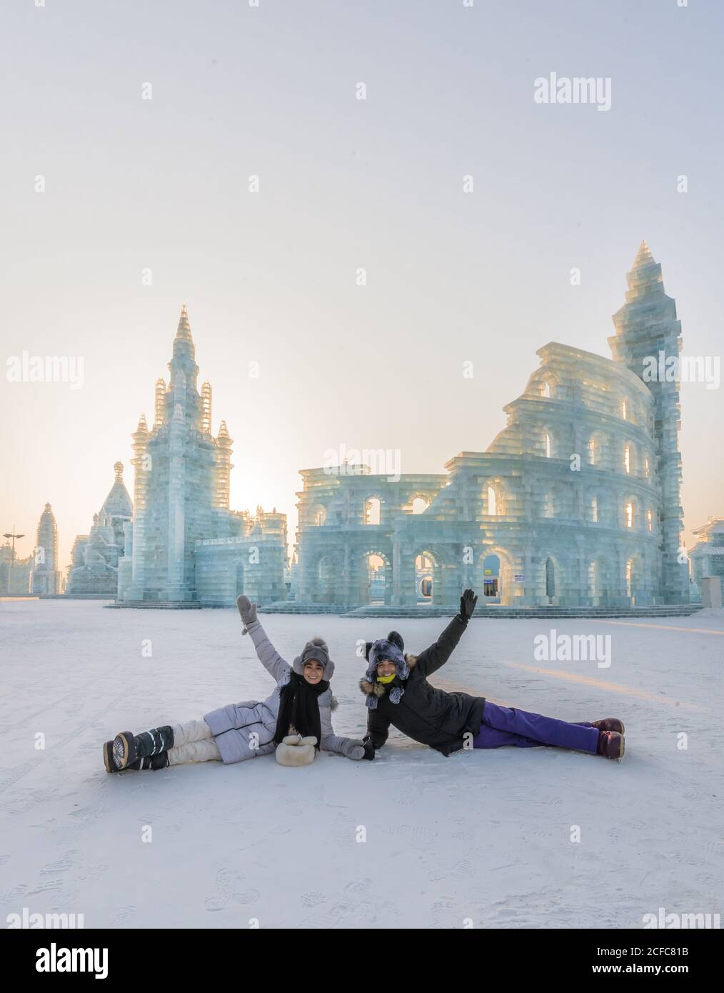 Felice giovane e donna in outwear alzando le armi, mentre si trova vicino al Colosseo e la costruzione del castello durante il ghiaccio e la scultura festival neve in inverno Foto Stock