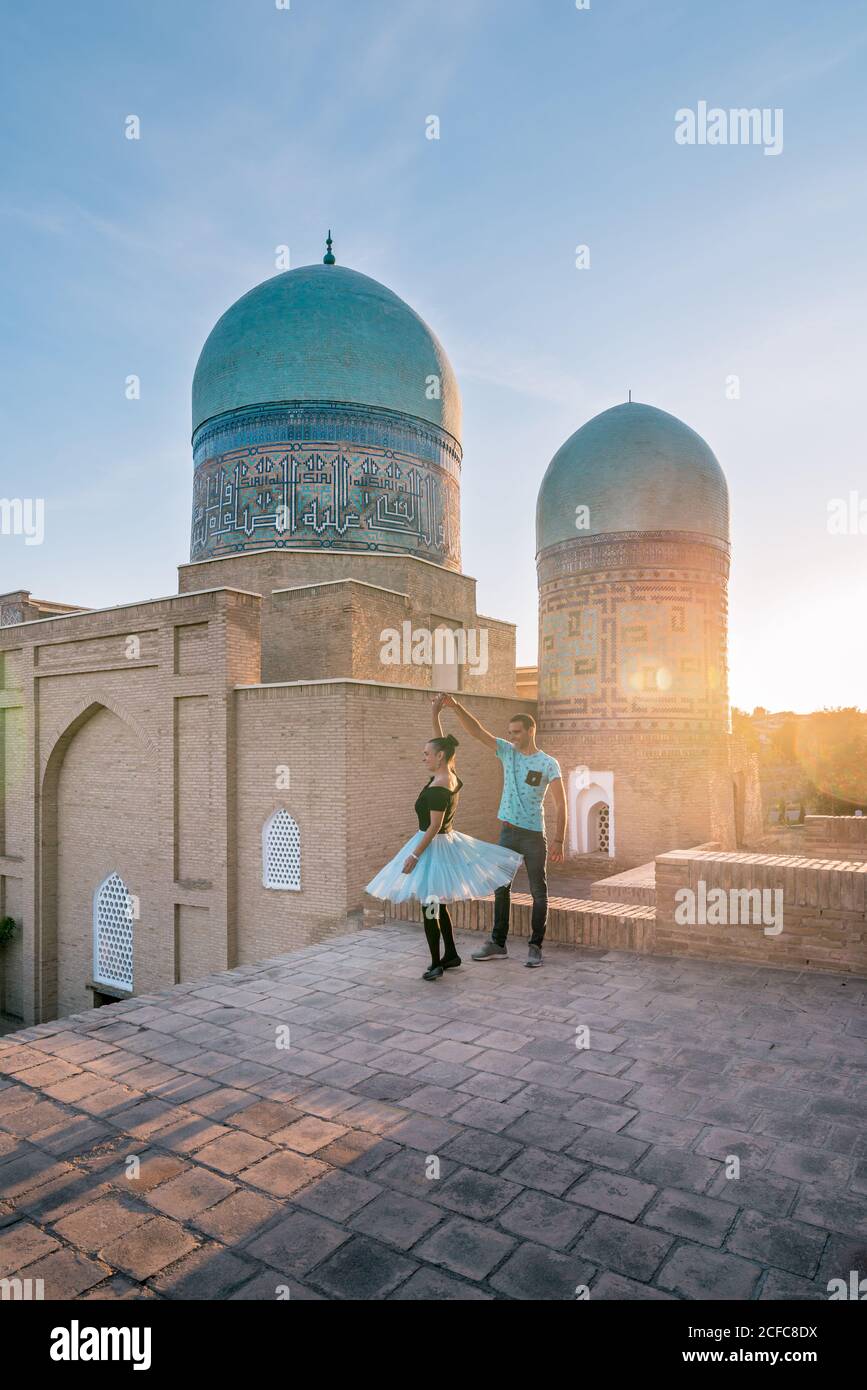 Uomo e donna a corpo pieno che ballano contro l'antico edificio islamico con cupole mentre visitano Shah-i-Zinda a Samarcanda, Uzbekistan Foto Stock
