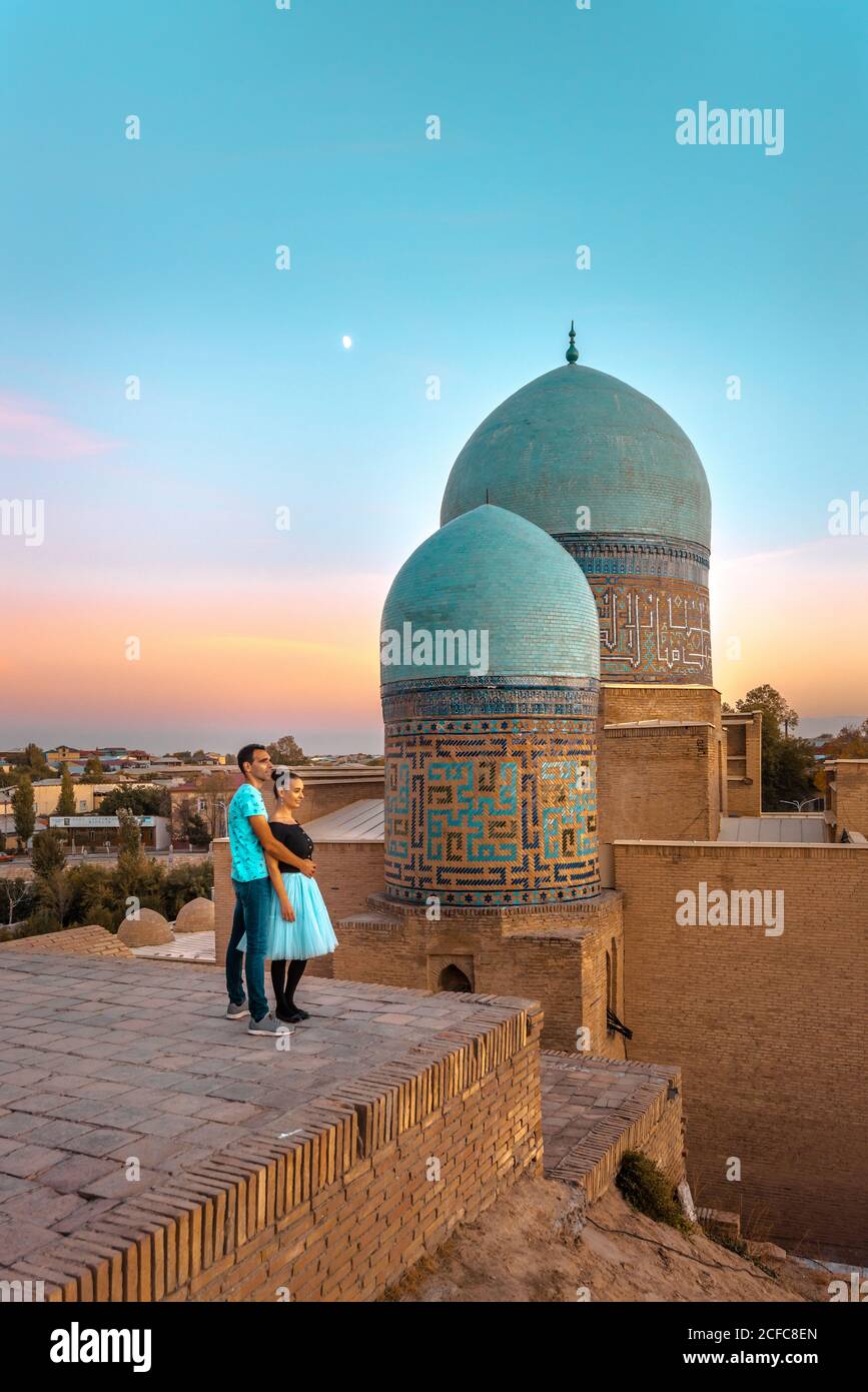 Una coppia si abbraccia vicino all'antico edificio islamico con cupole mentre si visita Shah-i-Zinda a Samarkand, Uzbekistan Foto Stock