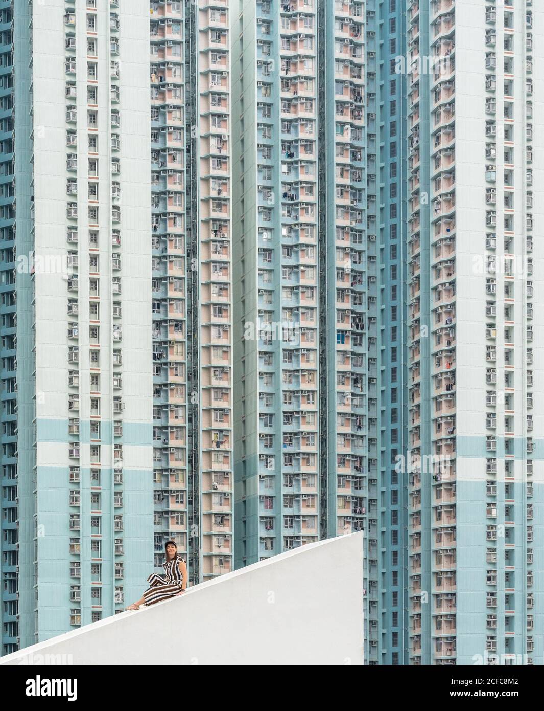 Donna rilassata in bianco e scuro abito a righe seduta su Tetto in cemento inclinato e guardando la macchina fotografica a Hong Kong In Cina Foto Stock