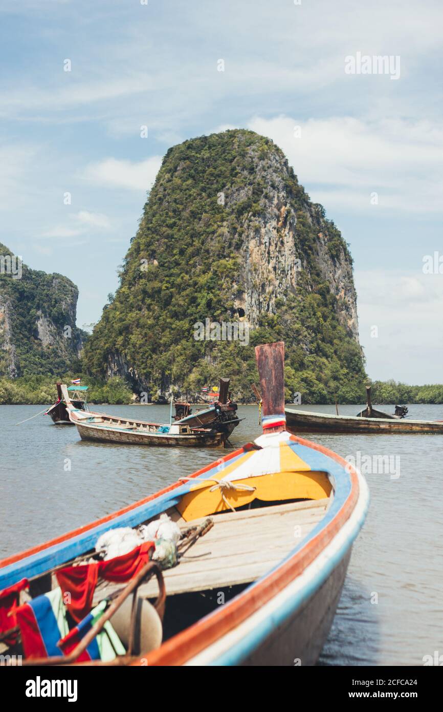 Barche di legno che galleggiano su acque tranquille della laguna con roccia verde sullo sfondo, Thailandia Foto Stock