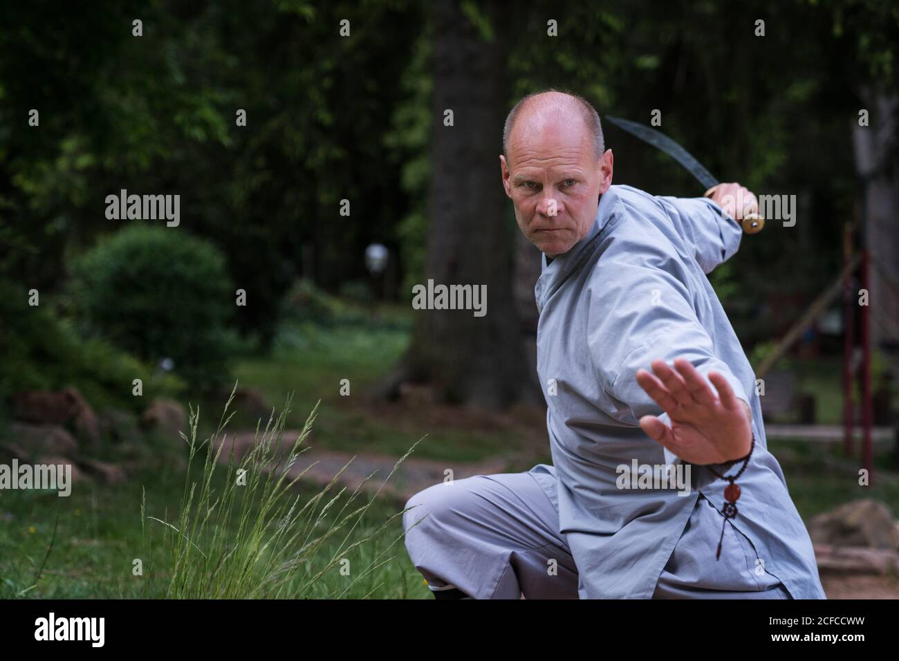 Determinato maschio di mezza età in kimono focalizzare e usando la spada mentre si allenano da soli in giardino Foto Stock