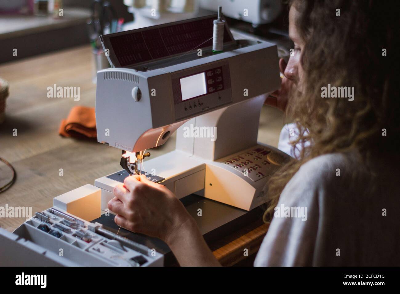 Vista posteriore del raccolto anonimo Donna con macchina da cucire che fa i vestiti seduti al tavolo in casa Foto Stock