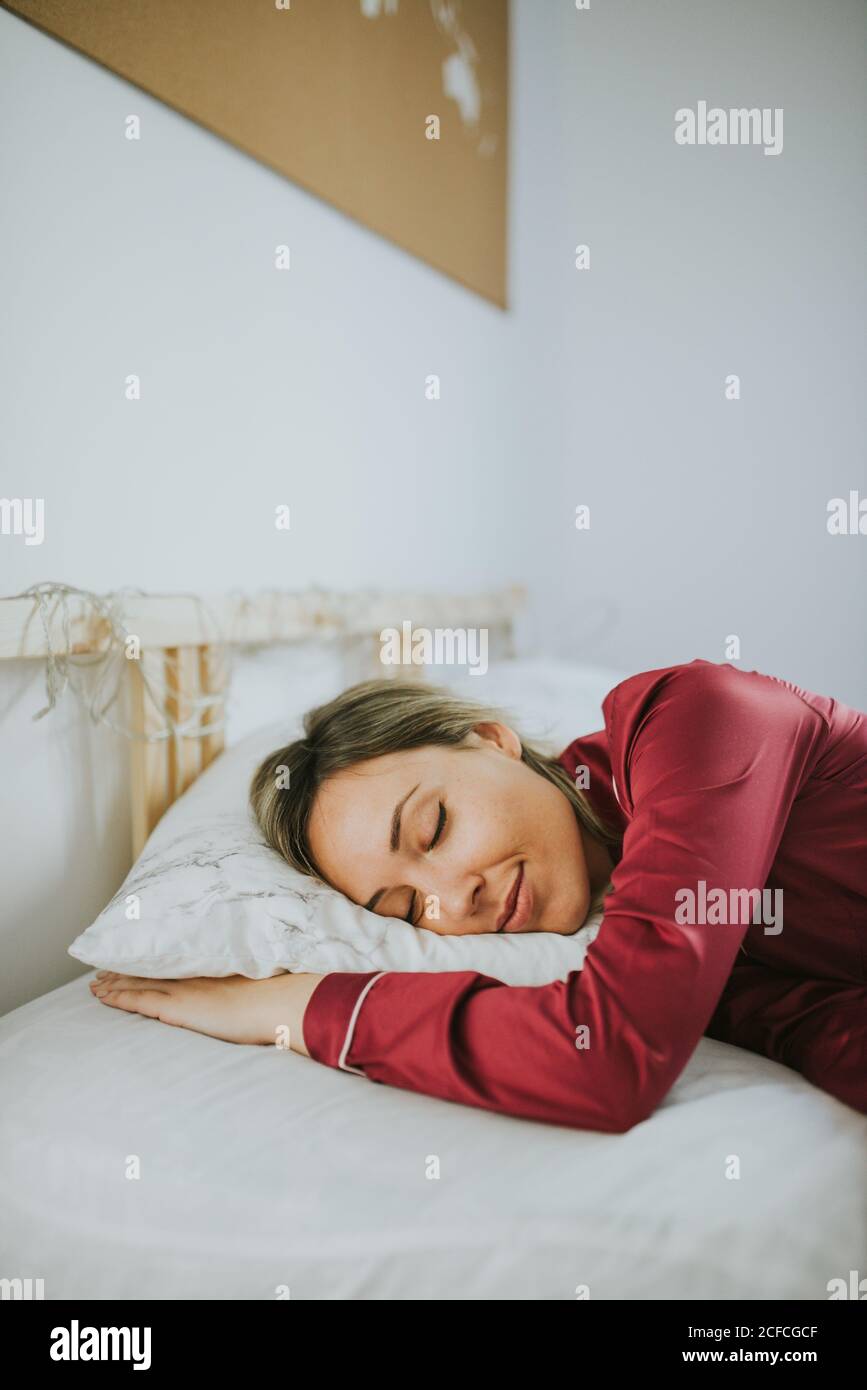 Giovane bella donna in pigiama sorridente mentre dormiva a letto in camera da letto Foto Stock