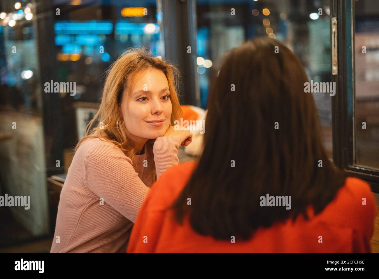 Giovani donne multirazziali sorridenti e che parlano tra loro sedersi al tavolo in un'accogliente caffetteria divertendosi Foto Stock