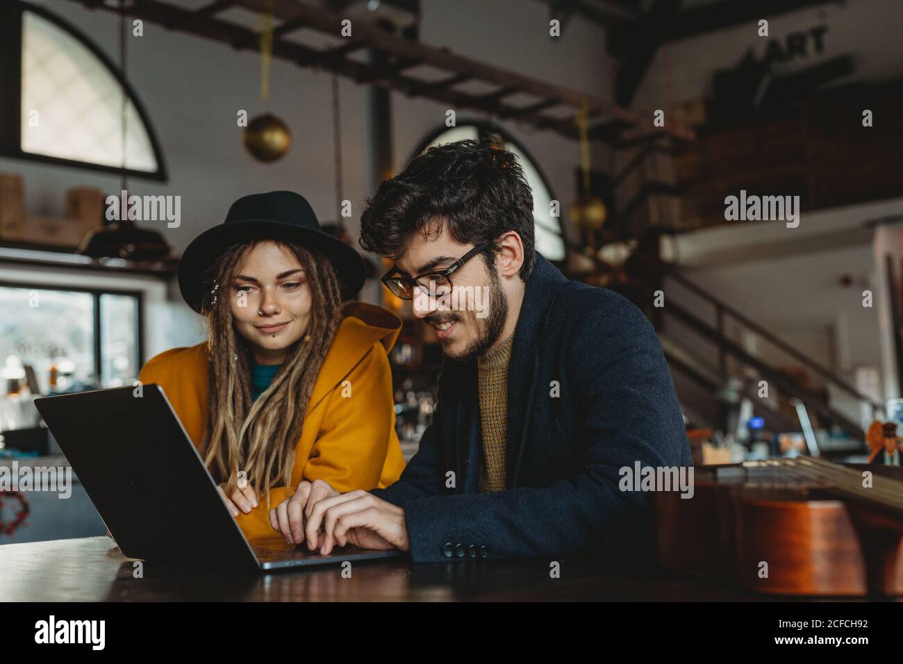 Uomo intelligente in occhiali e donna elegante in cappello al monitor  mentre l'uomo scrive sul computer portatile in caffetteria Foto stock -  Alamy