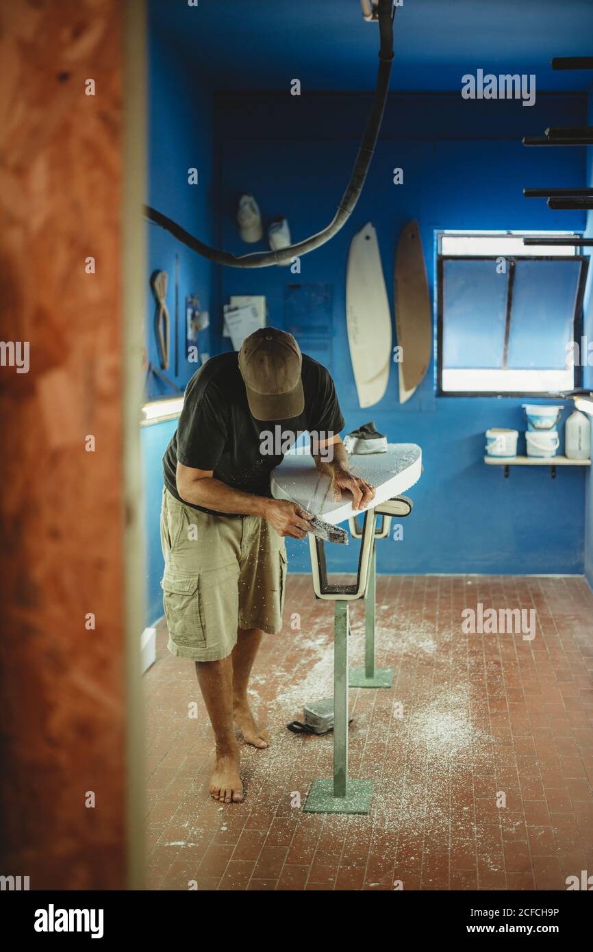 Woodworker che scuoiano diligentemente tavole da surf in officina Foto Stock