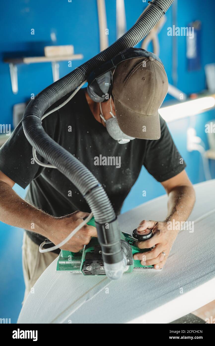 Operatore in maschera protettiva regolazione dettagli tavola da surf in officina Foto Stock