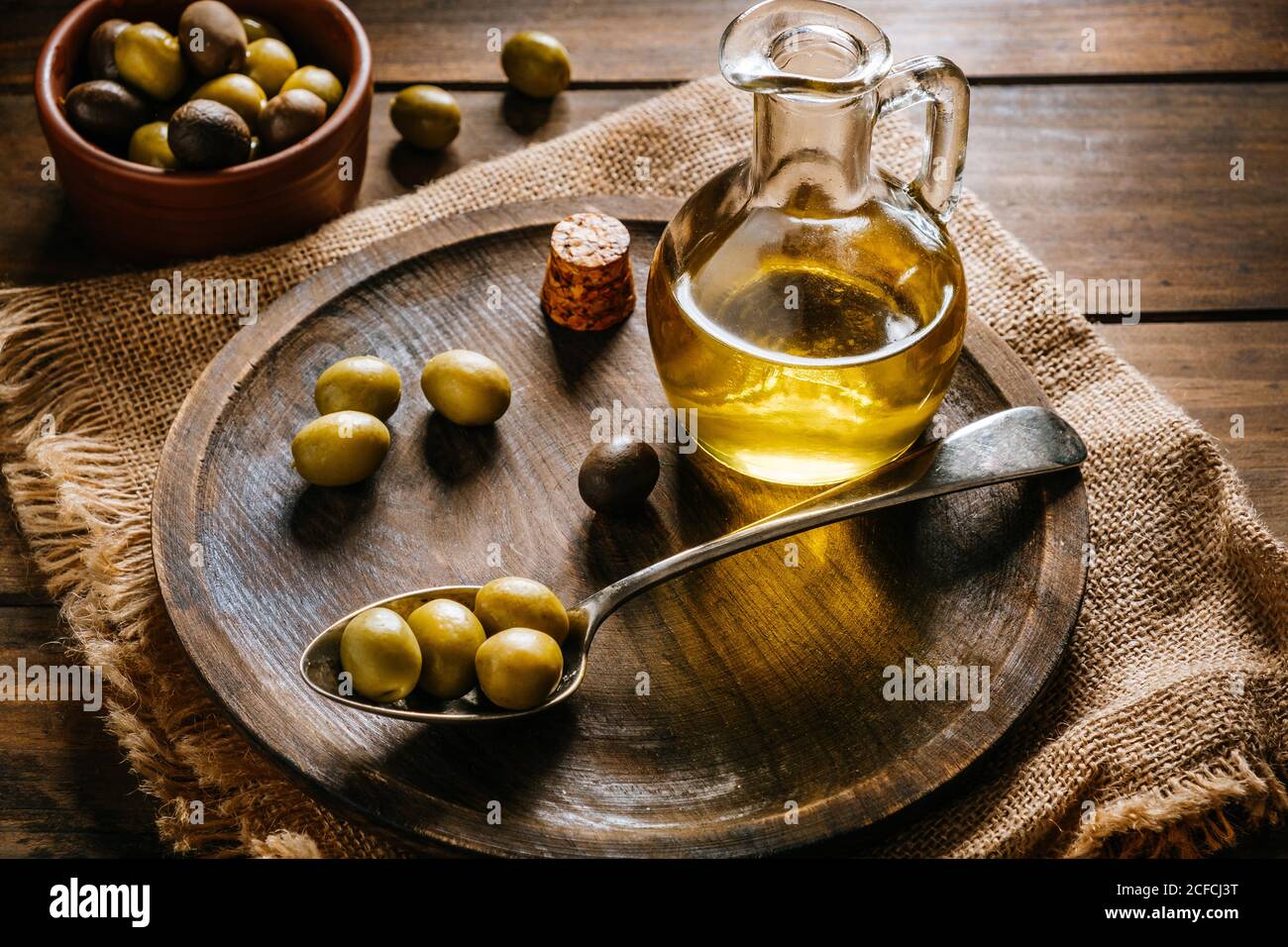 Da sopra vaso di vetro con olio extravergine posto sopra piatto di legno con olive nere e verdi Foto Stock