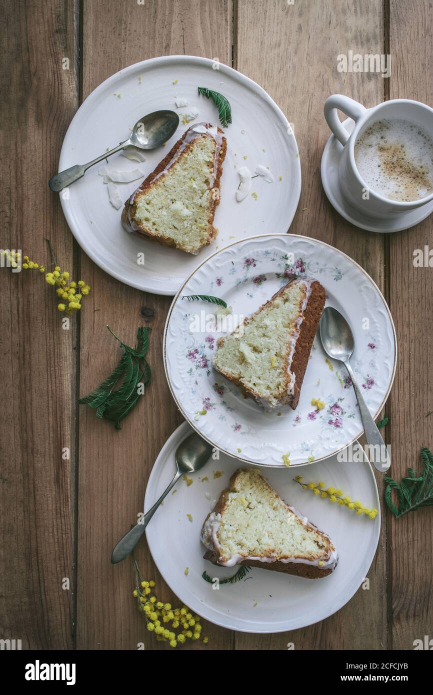 Vista dall'alto di fette di limone vegano fresco e cocco cake su piatti con cucchiai e tazza di caffè Foto Stock