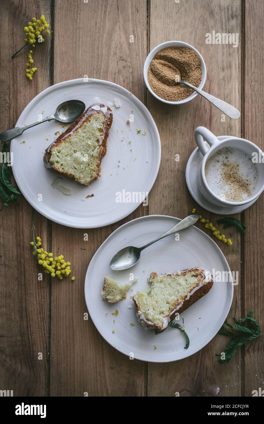 Vista dall'alto di fette di limone vegano fresco e cocco cake su piatti con cucchiai e tazza di caffè Foto Stock