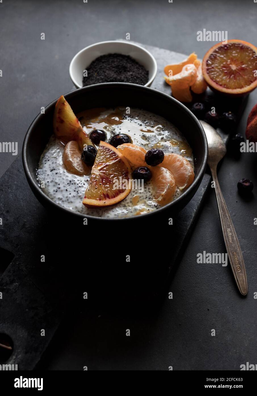 Dall'alto semi di chia pudding con fette di arancia, mandarini e olive in ciotola vicino al cucchiaio e pompelmo su tavola scura Foto Stock