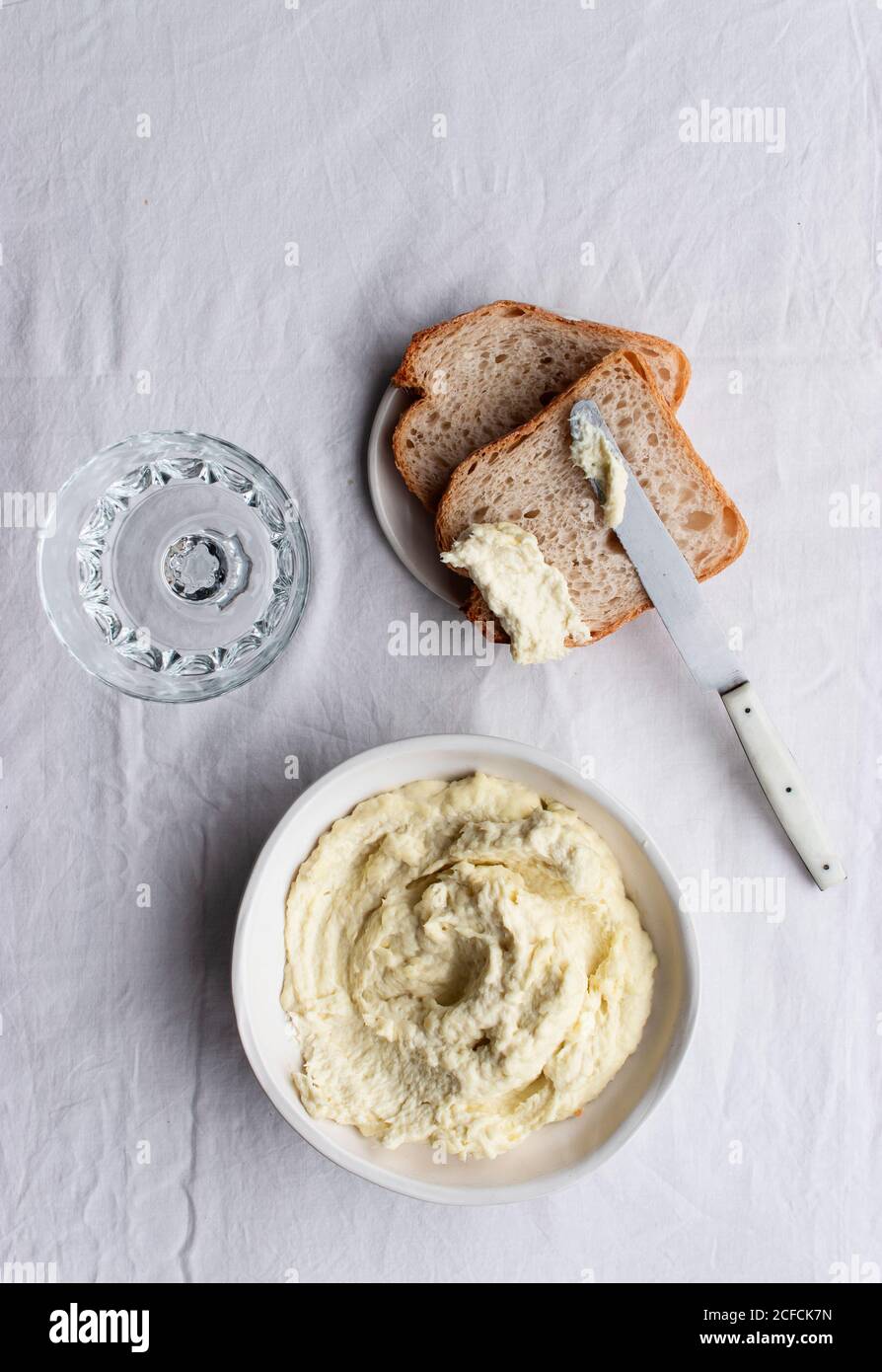 Da sopra ciotola con brandade di merluzzo posto vicino alle olive, fette di pane e foglie di alloro su un tavolo da cucina sfondo bianco Foto Stock