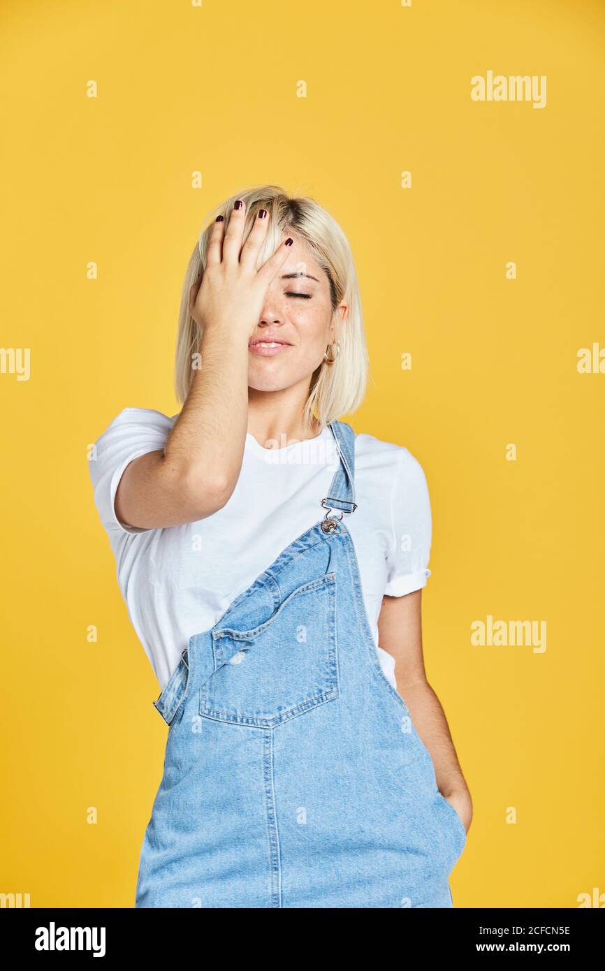 Bella giovane donna in t-shirt bianca e jeans sundress in piedi su sfondo giallo e guardando verso il basso Foto Stock