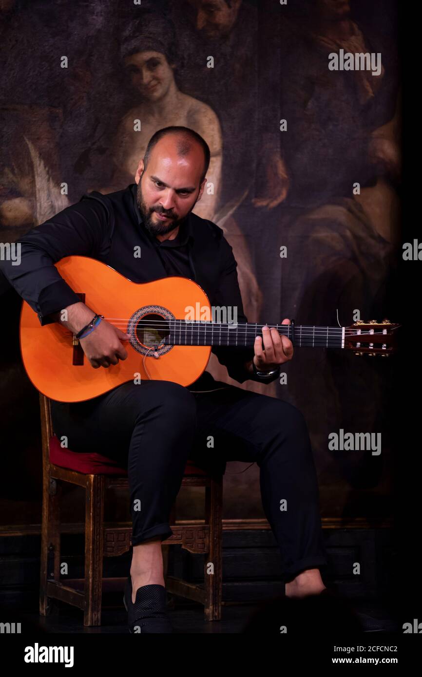 Un ragazzo calvo che suona la chitarra acustica mentre si siede sul palco durante lo spettacolo di flamenco Foto Stock