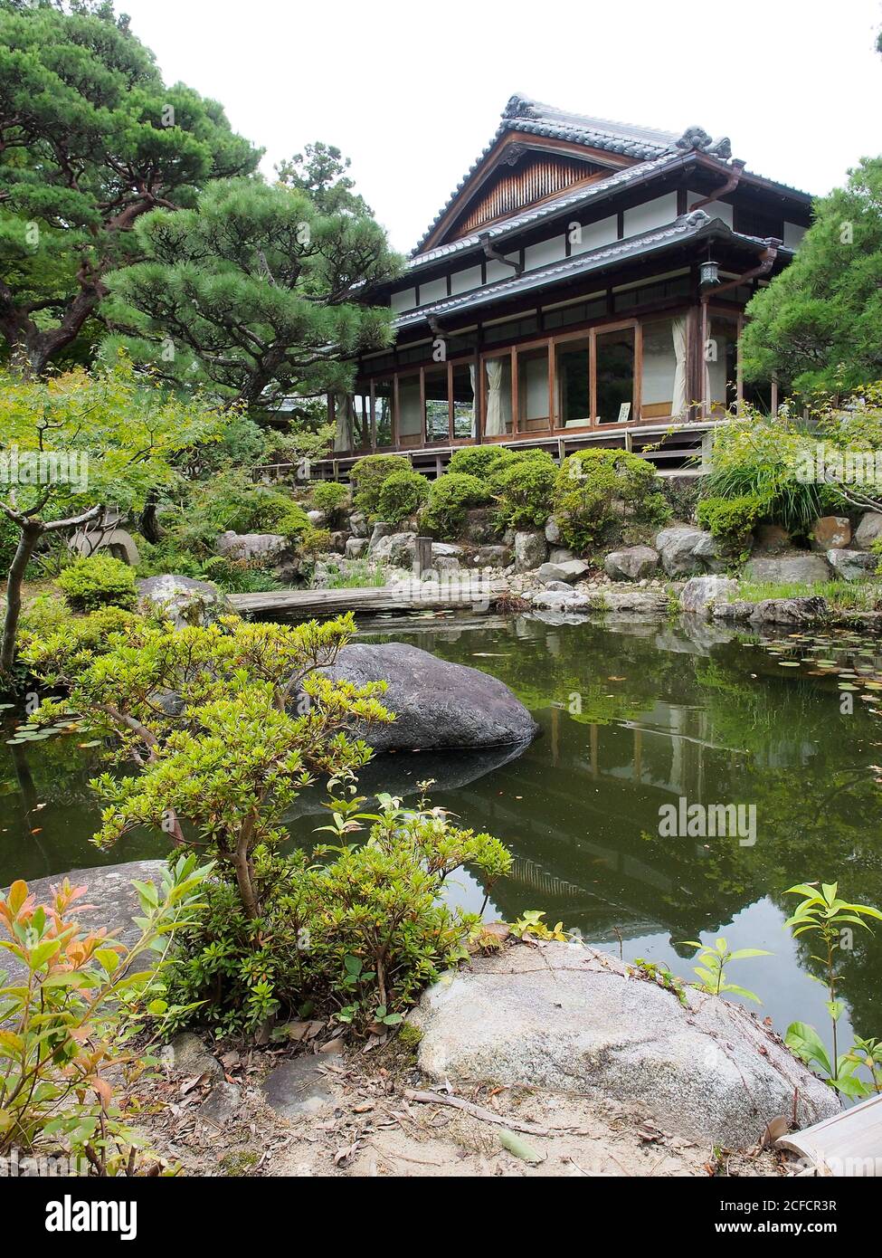 Stagno con acqua tranquilla circondato da cespugli verdi e situato In giardino al di fuori di autentica casa asiatica in Giappone Foto Stock