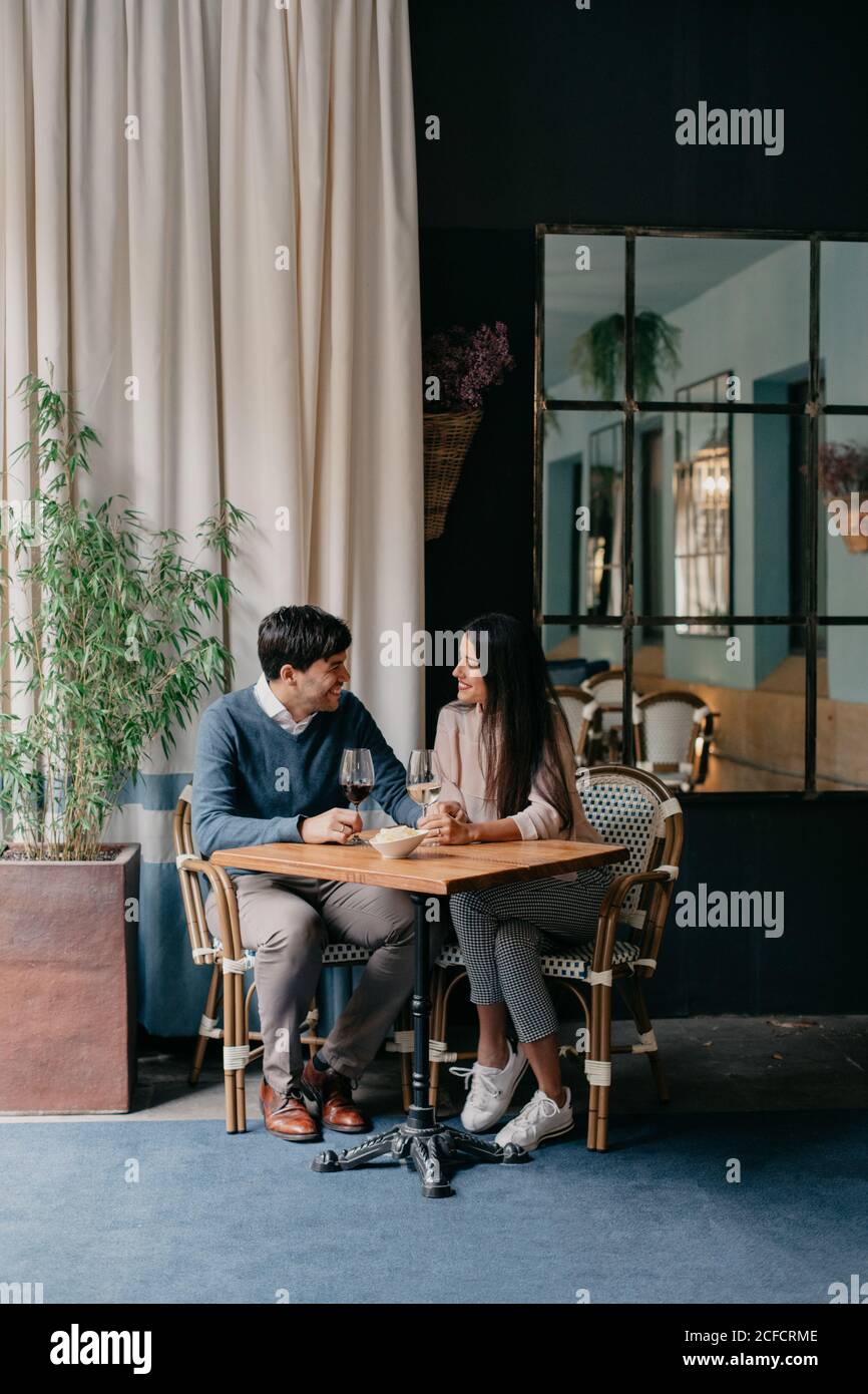 Felice giovane coppia affettuosa romantica con bicchieri di vino e. tenere le mani mentre si siede a un tavolo di legno in un'accogliente caffetteria Foto Stock