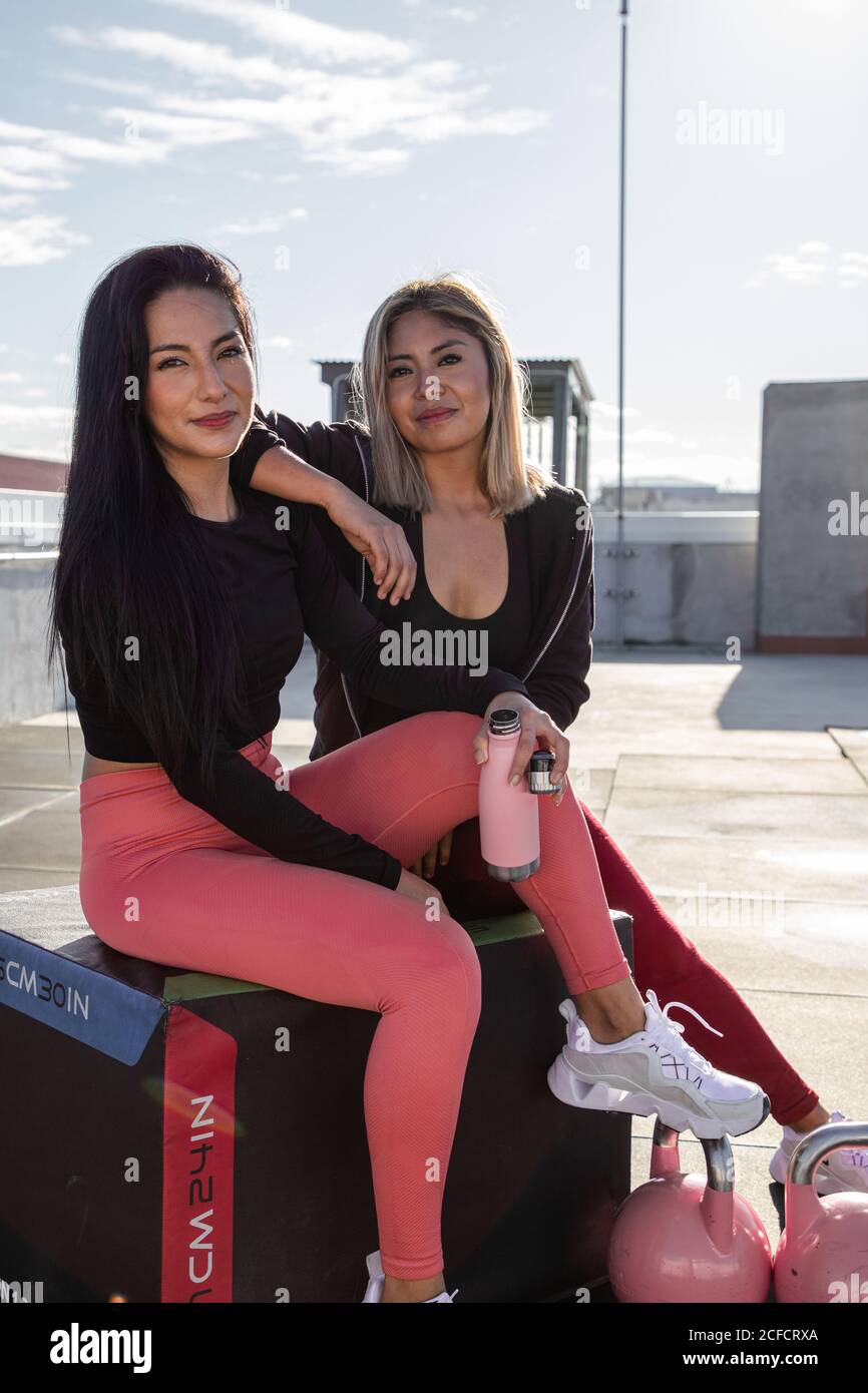 Belle amiche atletiche in abbigliamento attivo sorridente mentre si guarda alla macchina fotografica dopo l'allenamento sul tetto dell'edificio Foto Stock