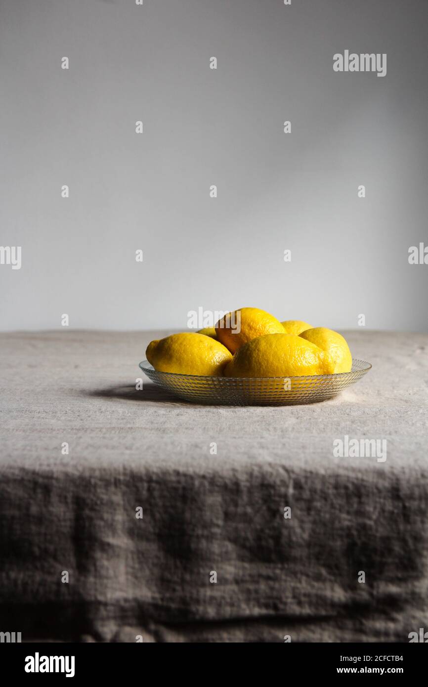 Limoni appetitosi con buccia gialla lucida in lastra di vetro sopra tovaglia di lino grigio Foto Stock