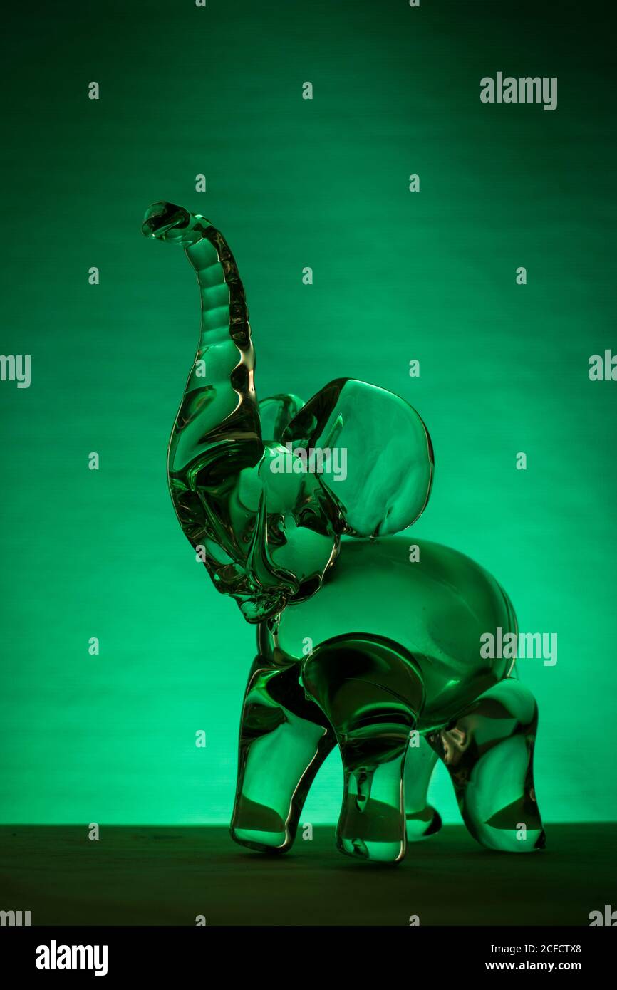 Elefante di vetro su un tavolo con luce verde sullo sfondo Foto Stock