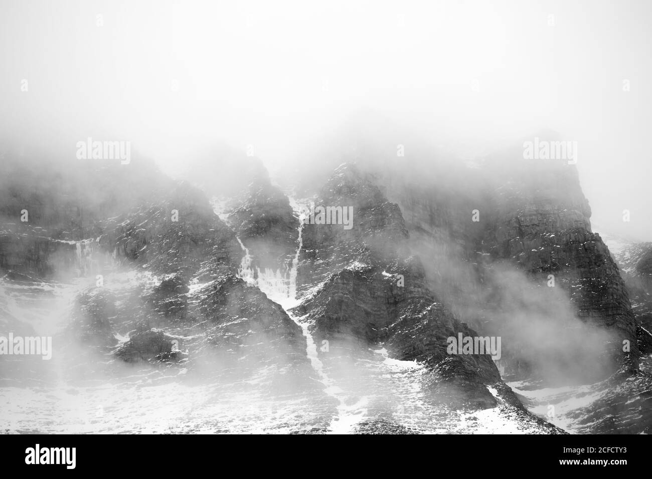 Fitte nuvole che galleggiano su cime di montagne innevate nelle maestose Dolomiti, Italia Foto Stock