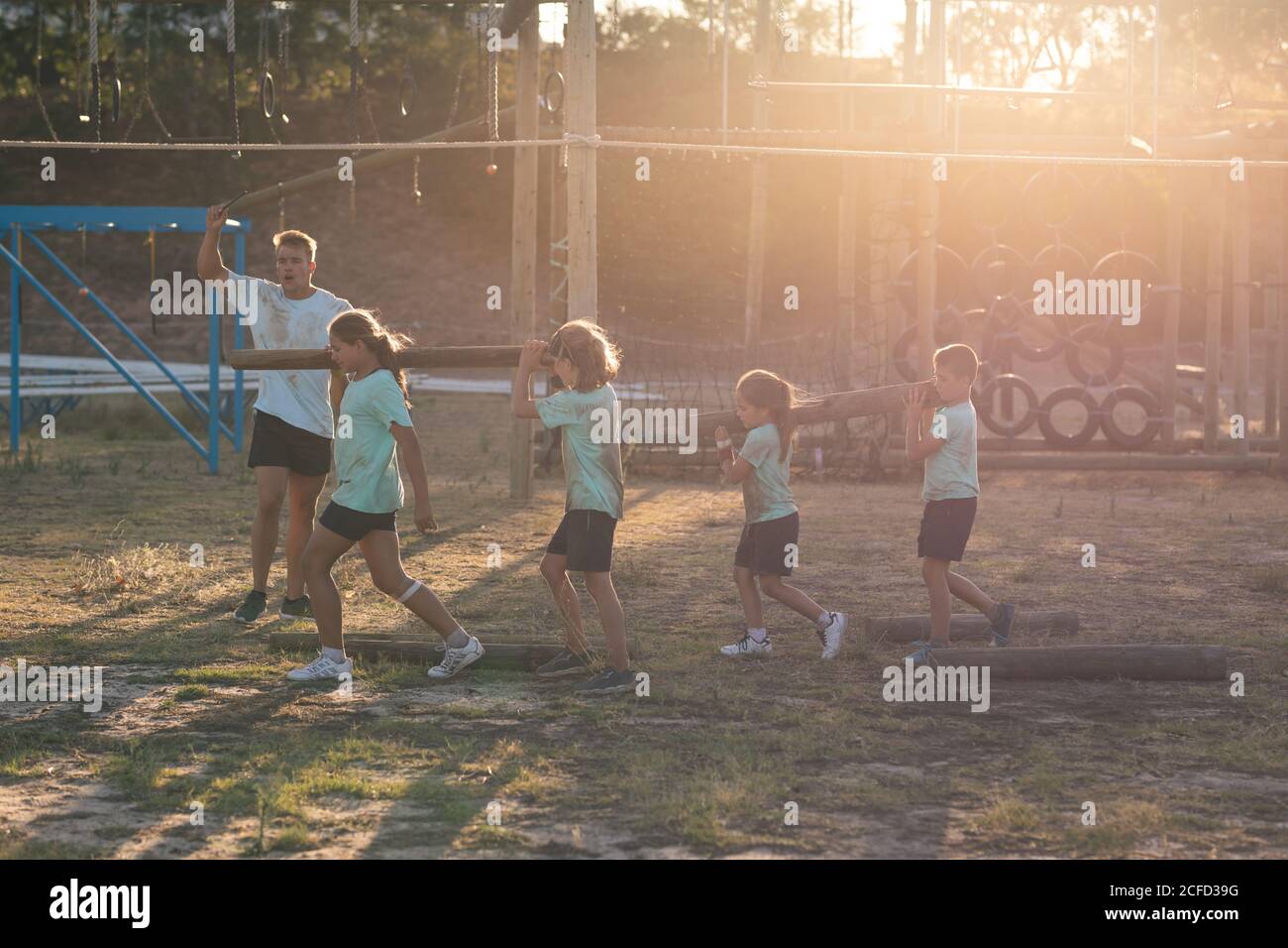 Allenatore di idoneità maschile istruendo mentre i bambini trasportano i registri ad un bootcamp Foto Stock