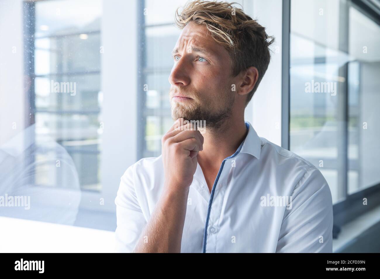 Pensieroso giovane uomo d'affari che guarda fuori dalla finestra dell'ufficio moderno Foto Stock