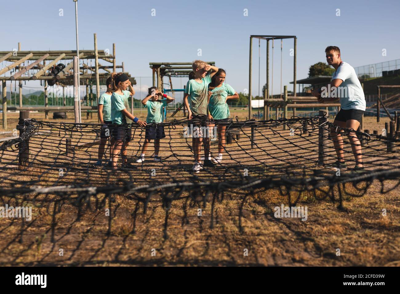 Allenatore di fitness maschile e bambini in piedi sulla rete di corda a. un campo di stivali Foto Stock