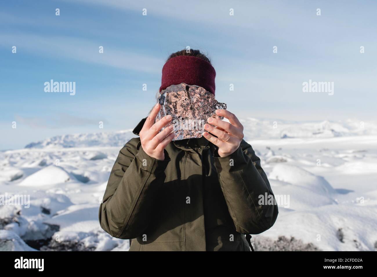 La donna tiene un piccolo pezzo di ghiaccio davanti al viso, Black Diamond Beach con le sue eponimi formazioni di ghiaccio, Islanda Foto Stock