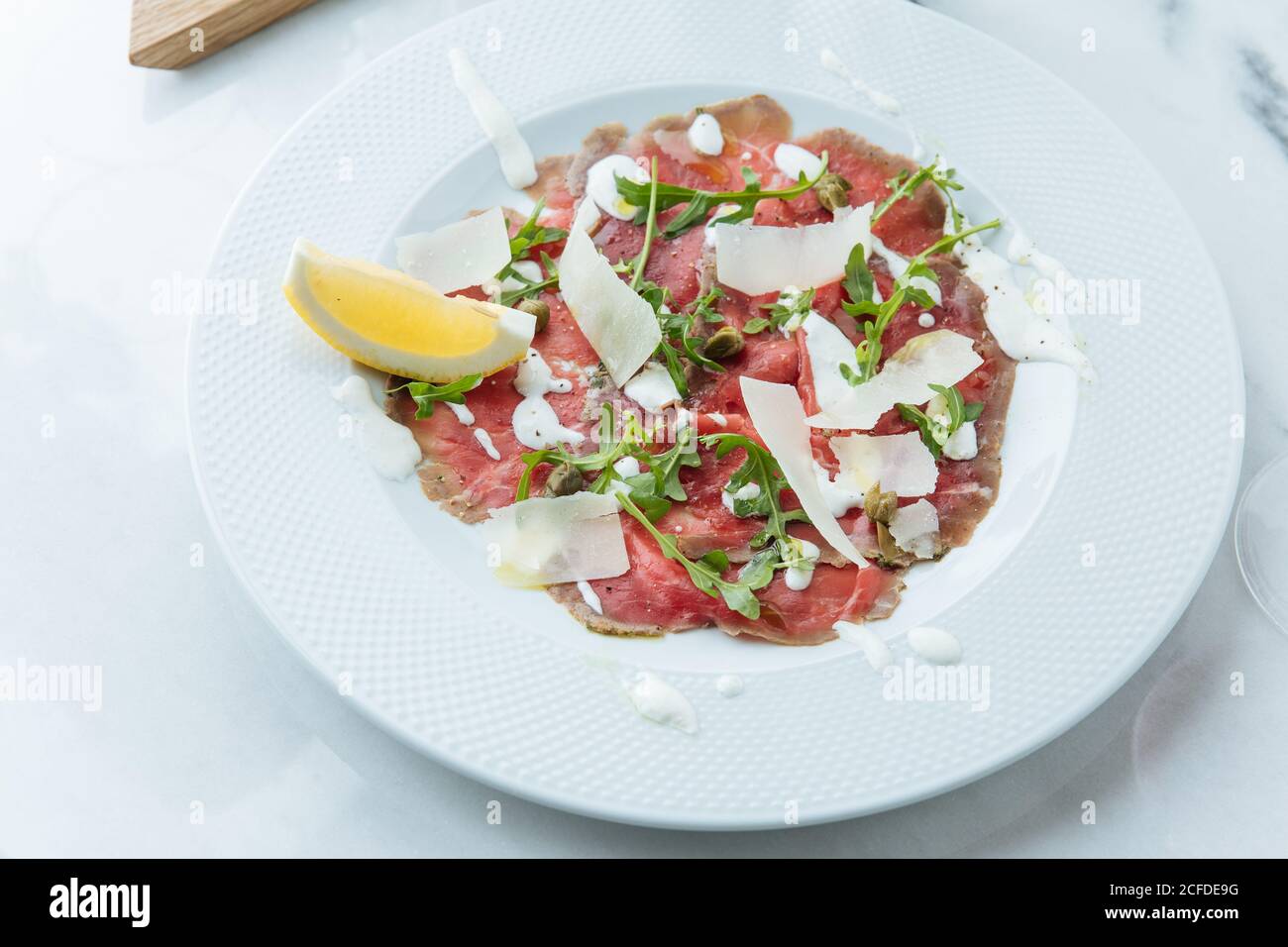 Dall'alto di fette di manzo rosso su piatto con pezzi di limone fresco decorato con salsa di formaggio bianco e rucola Foto Stock