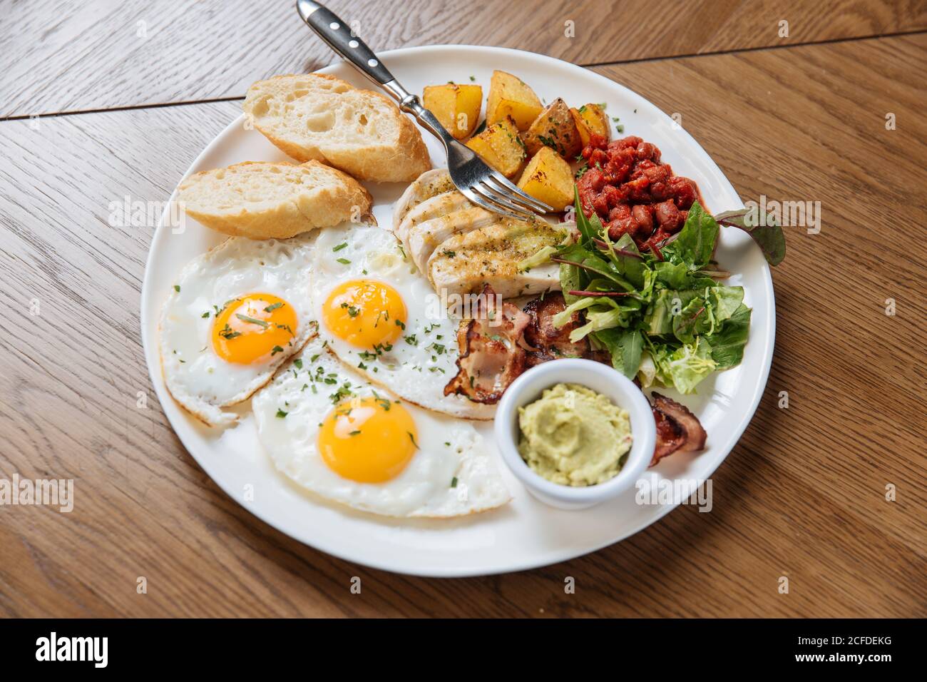 Vista dall'alto della colazione inglese servita con uova fritte e. pancetta con toast e verdure su tavolo di legno Foto Stock