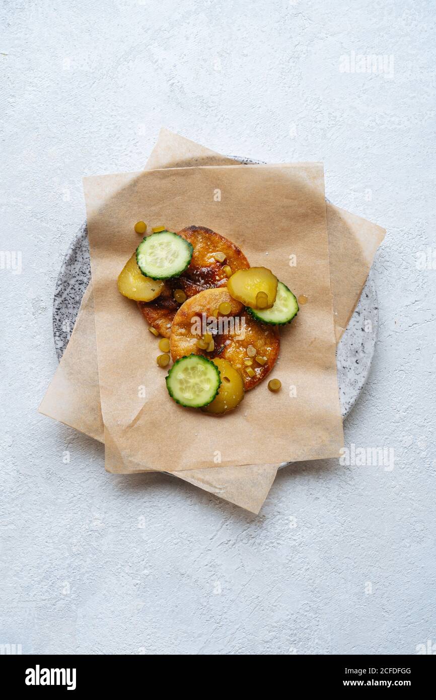 Vista dall'alto della salsa dorata sulla piastra con carta da forno decorato con fette di verde fresco e cetrioli sottaceto tabella Foto Stock