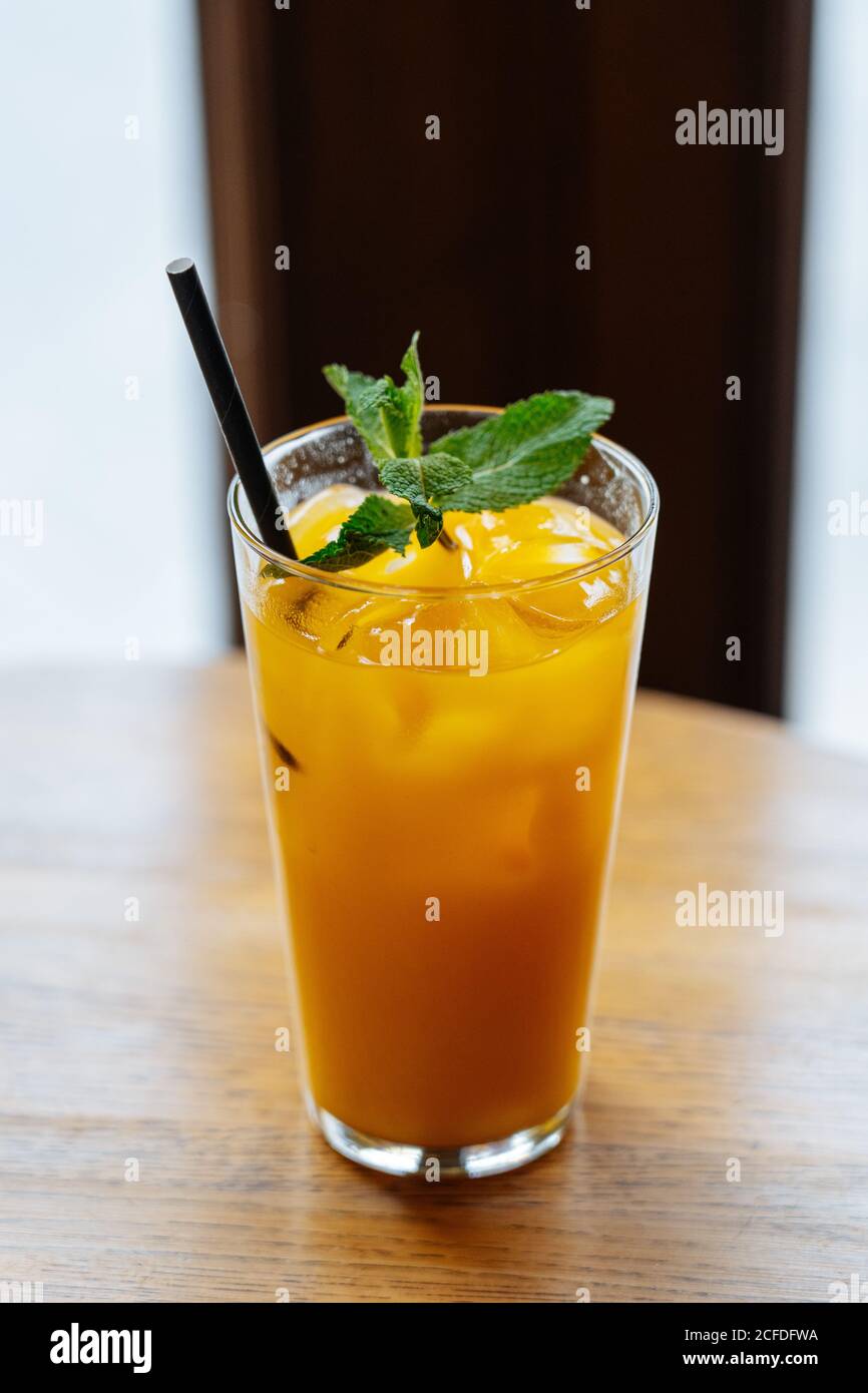 Dall'alto di deliziosa bevanda gialla in vetro di highball con ghiaccio decorato con menta verde fresca su tavolo in legno ristorante Foto Stock