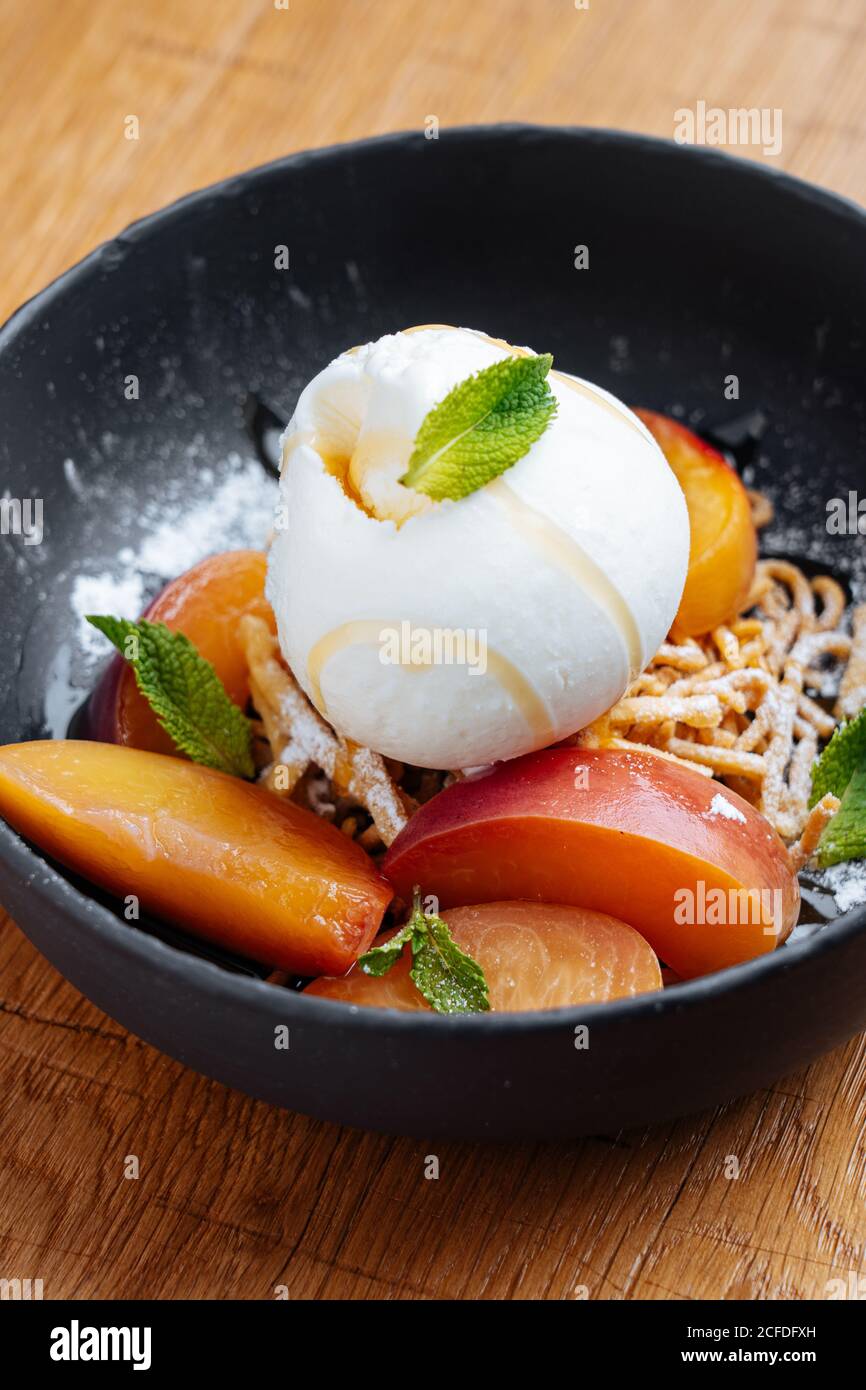 Dall'alto di fette fresche di mango con ghiaccio cremoso spaghetti crema e dolce decorati con menta in elegante nero ciotola Foto Stock