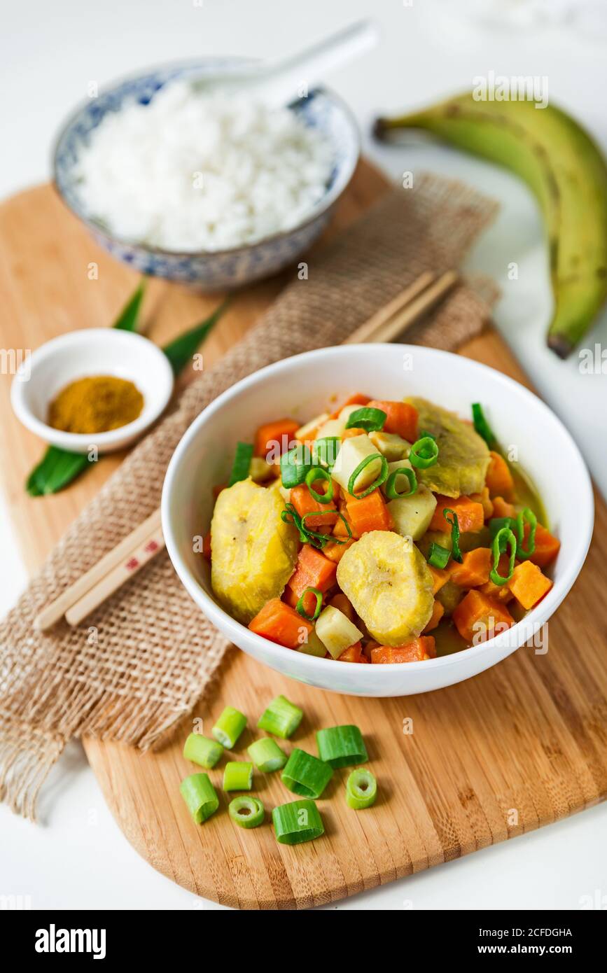 Curry asiatico con plantain e una ciotola di riso bianco su tavola di legno con bacchette e decorazioni Foto Stock
