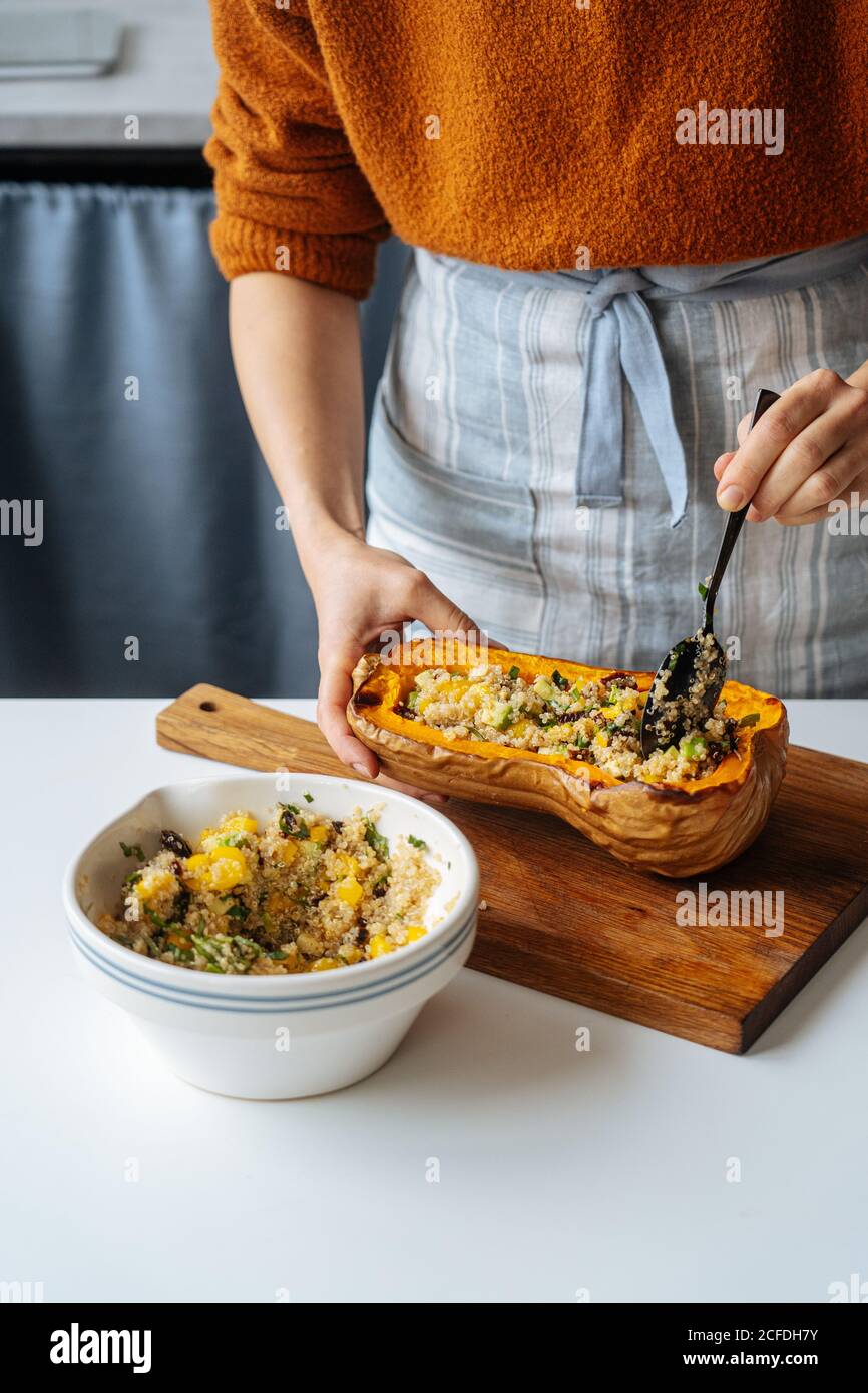 Crop casalinga ripieno di zucca di butternut al forno con miscela vegetariana di quinoa e verdure a tavola bianca in cucina casalinga Foto Stock