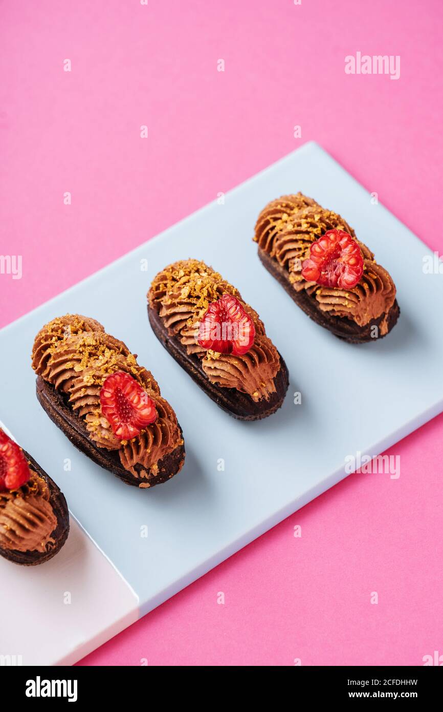 Dall'alto deliziosi lecci al cioccolato con pezzi di lamponi freschi e crema di caramello messo in linea a bordo su rosa sfondo Foto Stock